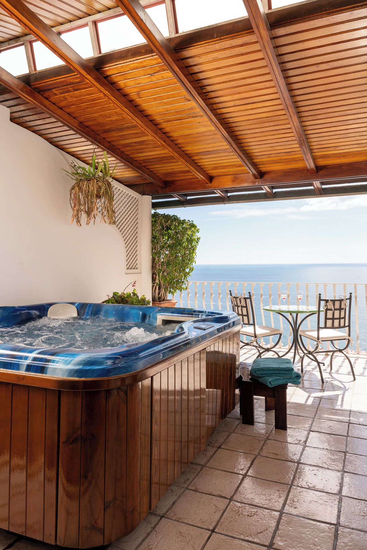 Un bain à remous avec un revêtement extérieur en bois, une table avec des chaises et une vue sur l’océan.