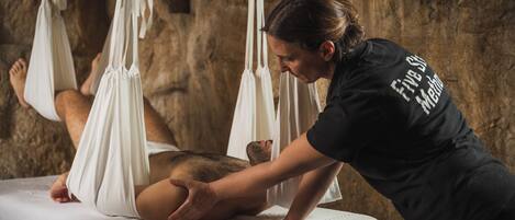 A person receiving a massage in a room with a stone wall and a massage table.