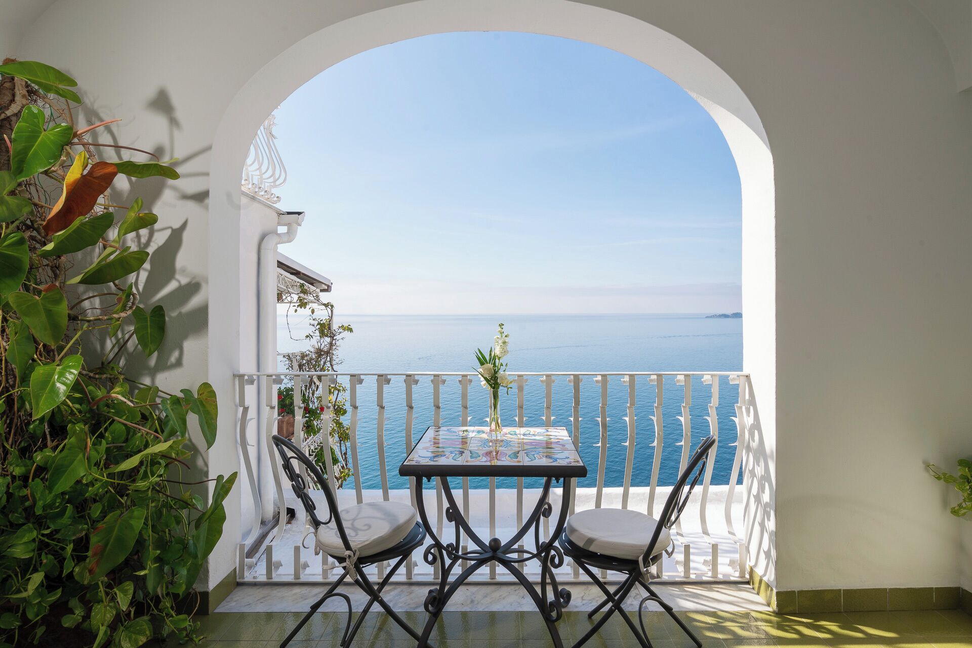 A balcony with a table and chairs, overlooking a sea view.
