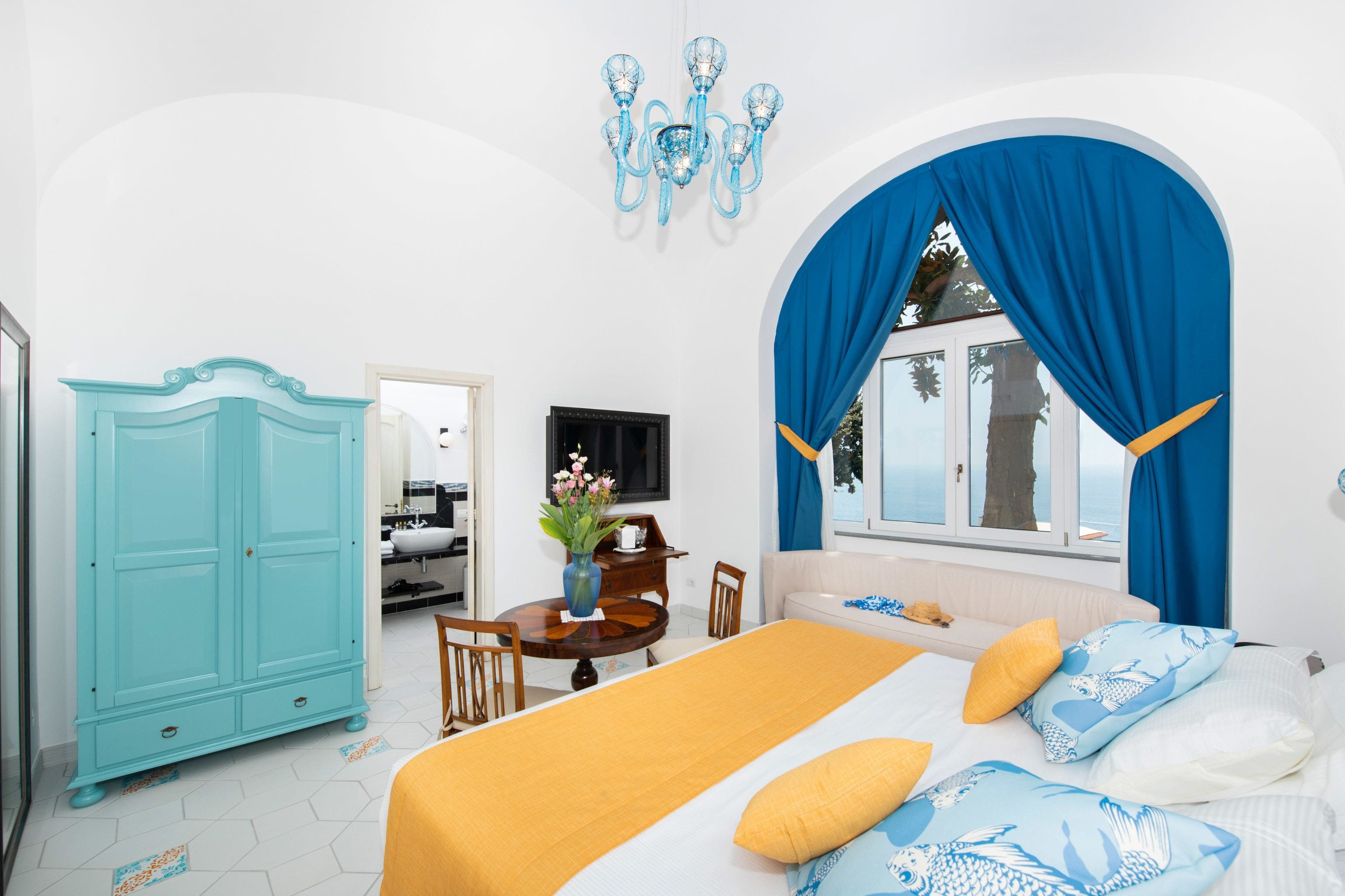 A bedroom with a bed, a blue arched window, a white wall, and a blue chandelier.