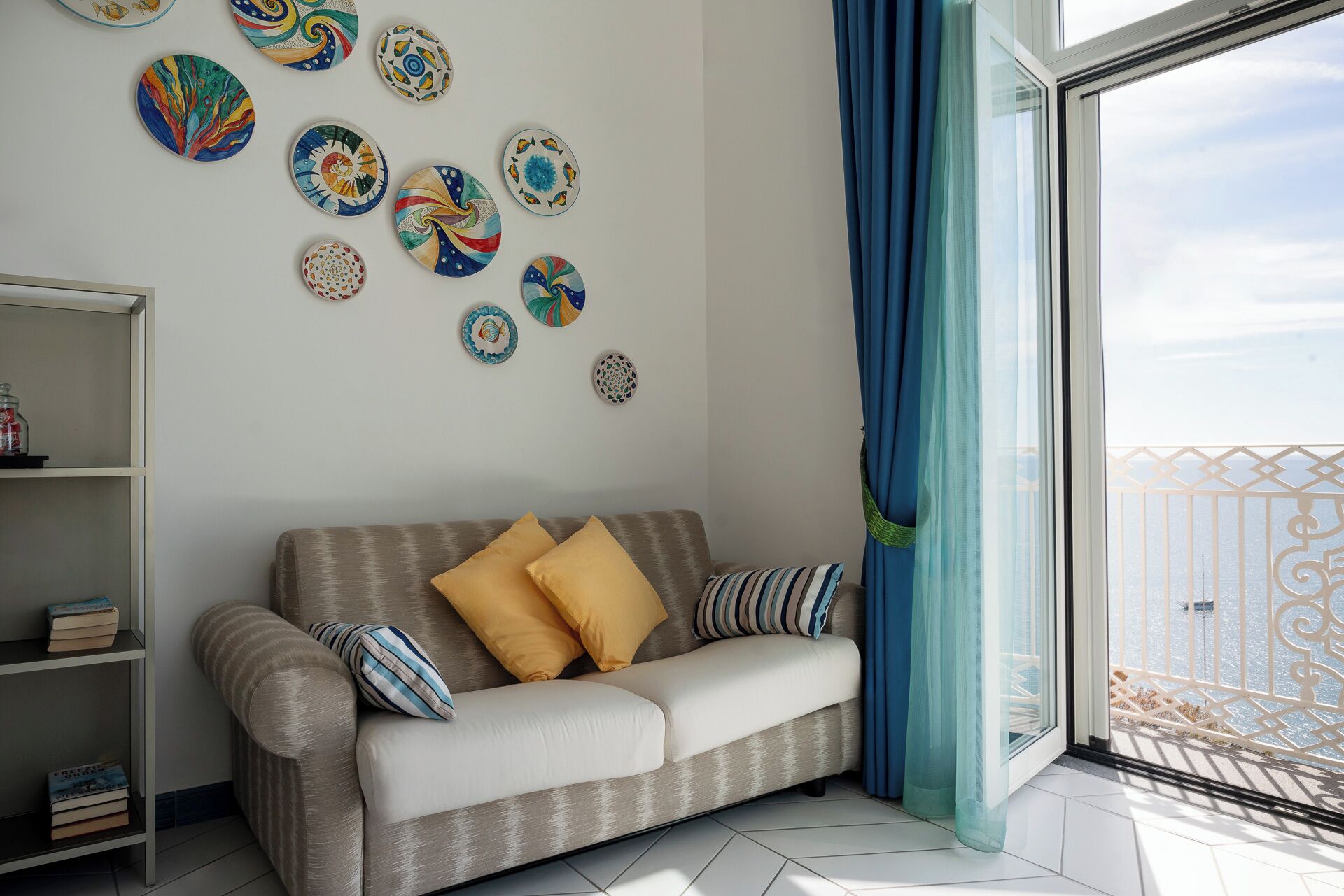 Ein Wohnzimmer mit Sofa, Kissen, einem Bücherregal und dekorativen Tellern an der Wand.
