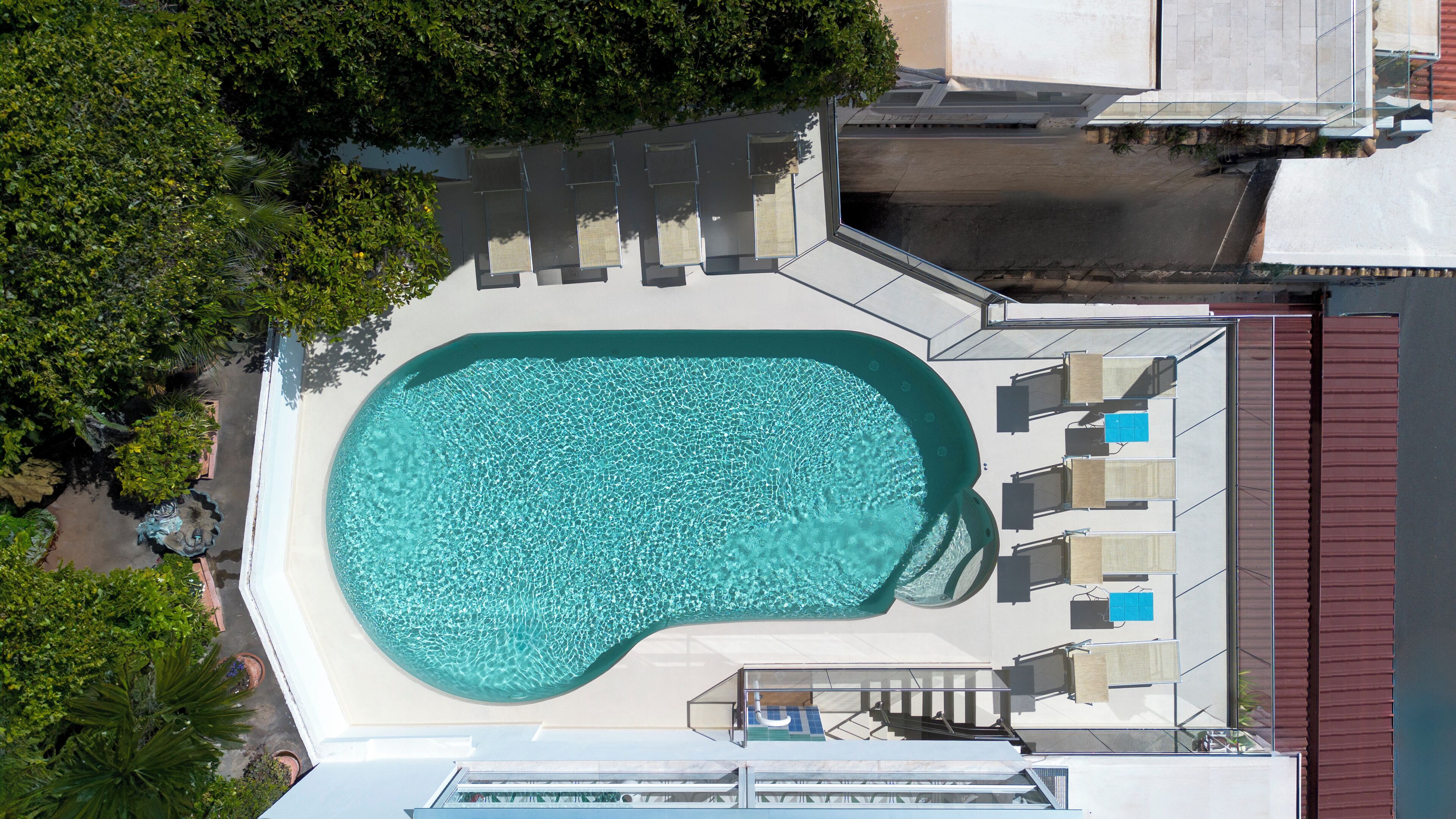 An aerial view of a swimming pool with a sunken center, surrounded by lounge chairs and a glass balustrade.