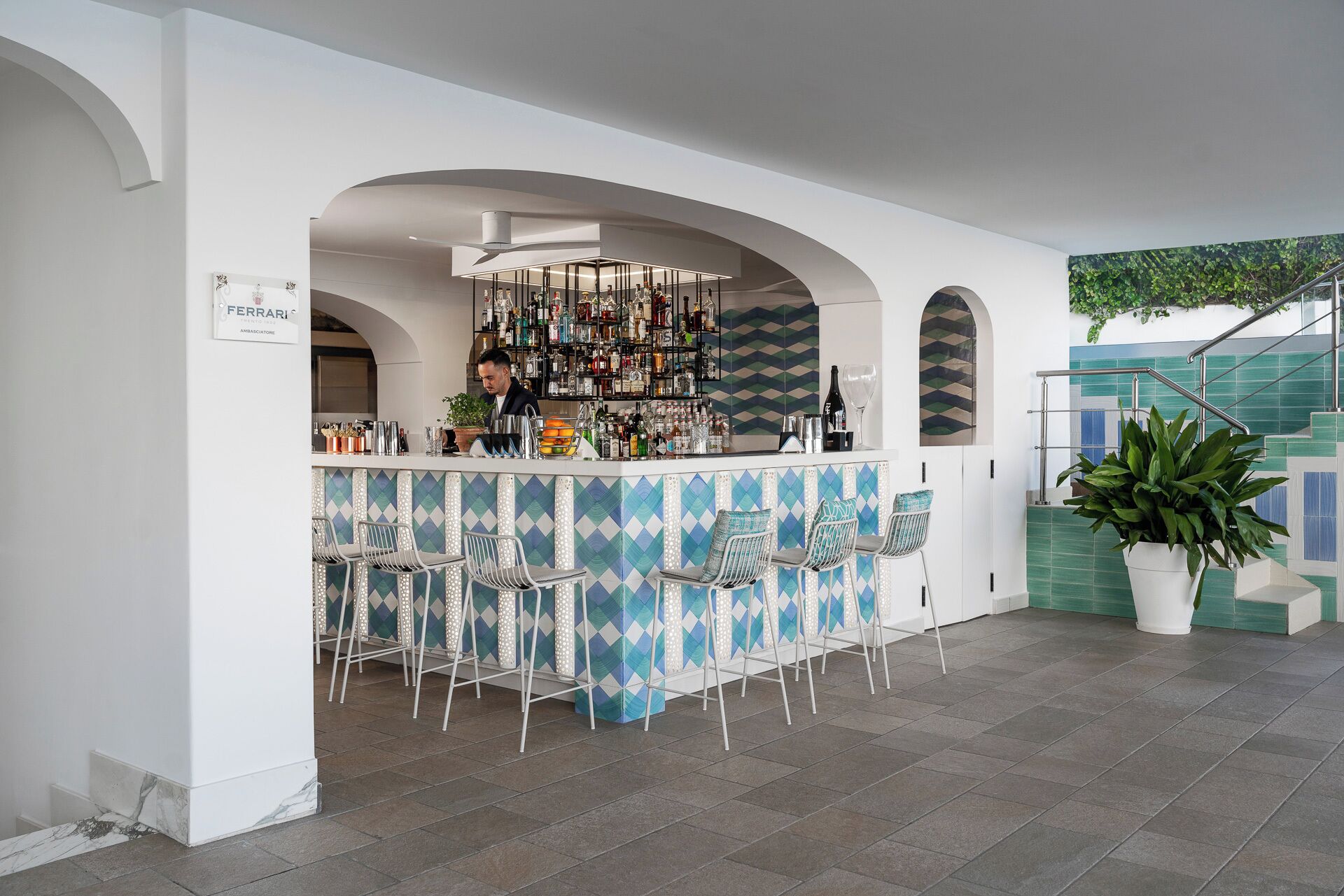 A bar area with a bartender, a well-stocked shelf of bottles, and a seating arrangement with chairs.