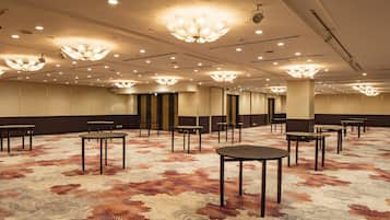 A spacious room with multiple tables and chairs, a patterned carpet, and ornate ceiling lights.