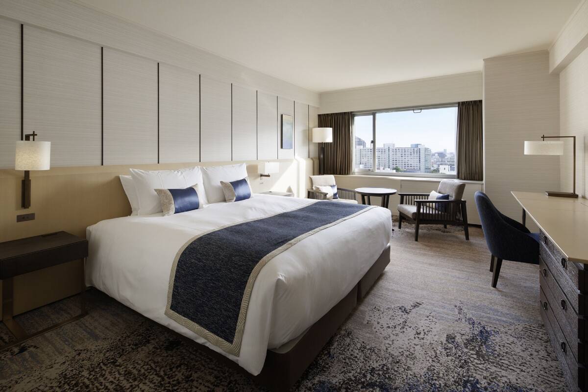 A hotel room with a large bed, a desk, a chair, and a view of the city.