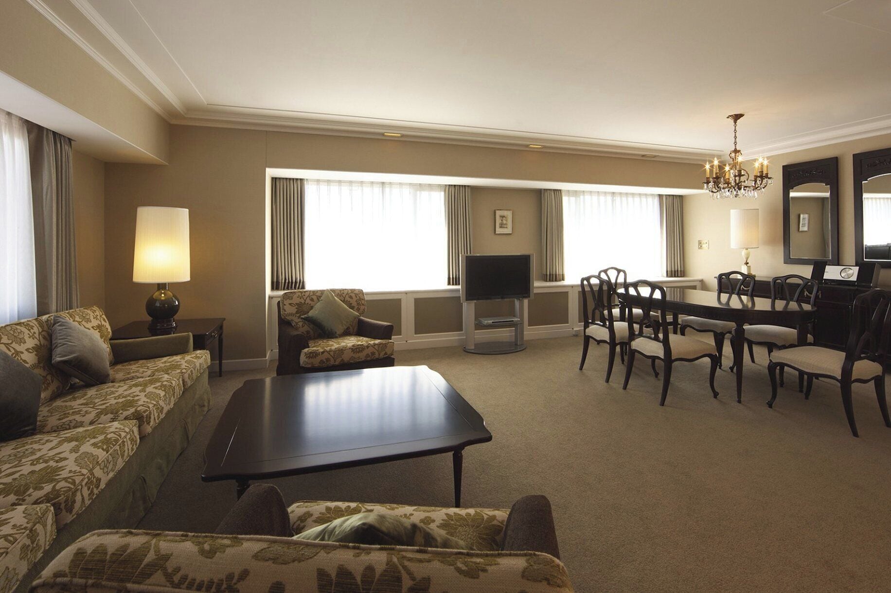 Une chambre d’hôtel comprenant un canapé, une table basse, un téléviseur, une table à manger avec des chaises et un lustre.