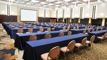 Une salle de conférence avec des rangées de tables et de chaises, un grand écran et un sol recouvert de moquette.