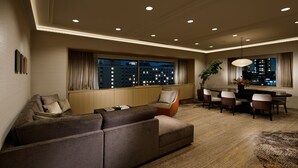 A modern living room with a sectional sofa, dining table with chairs, and a large window with a city view.