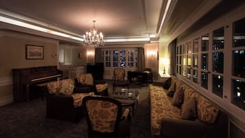 A spacious living room with a grand chandelier, a piano, and a sofa set.