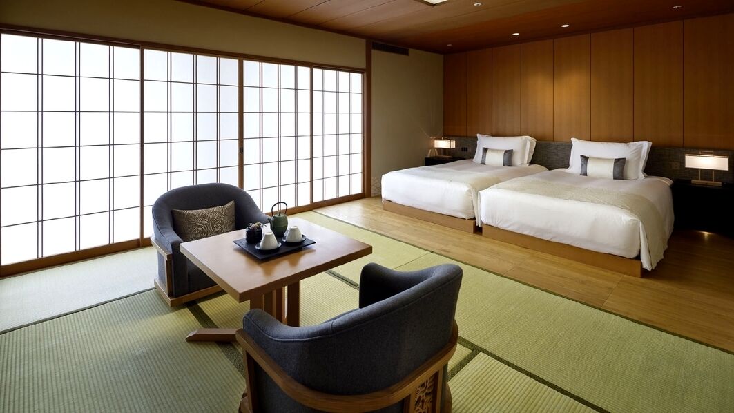 Een traditionele Japanse hotelkamer met tatami vloeren, een laag houten bed, een tafel met tatami mat en een verschuifbare shoji scherm.