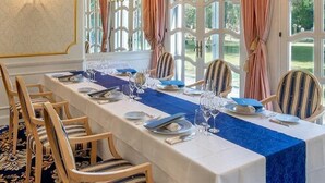 A formal dining room with a long table set for a meal, large windows with curtains, and a chandelier.