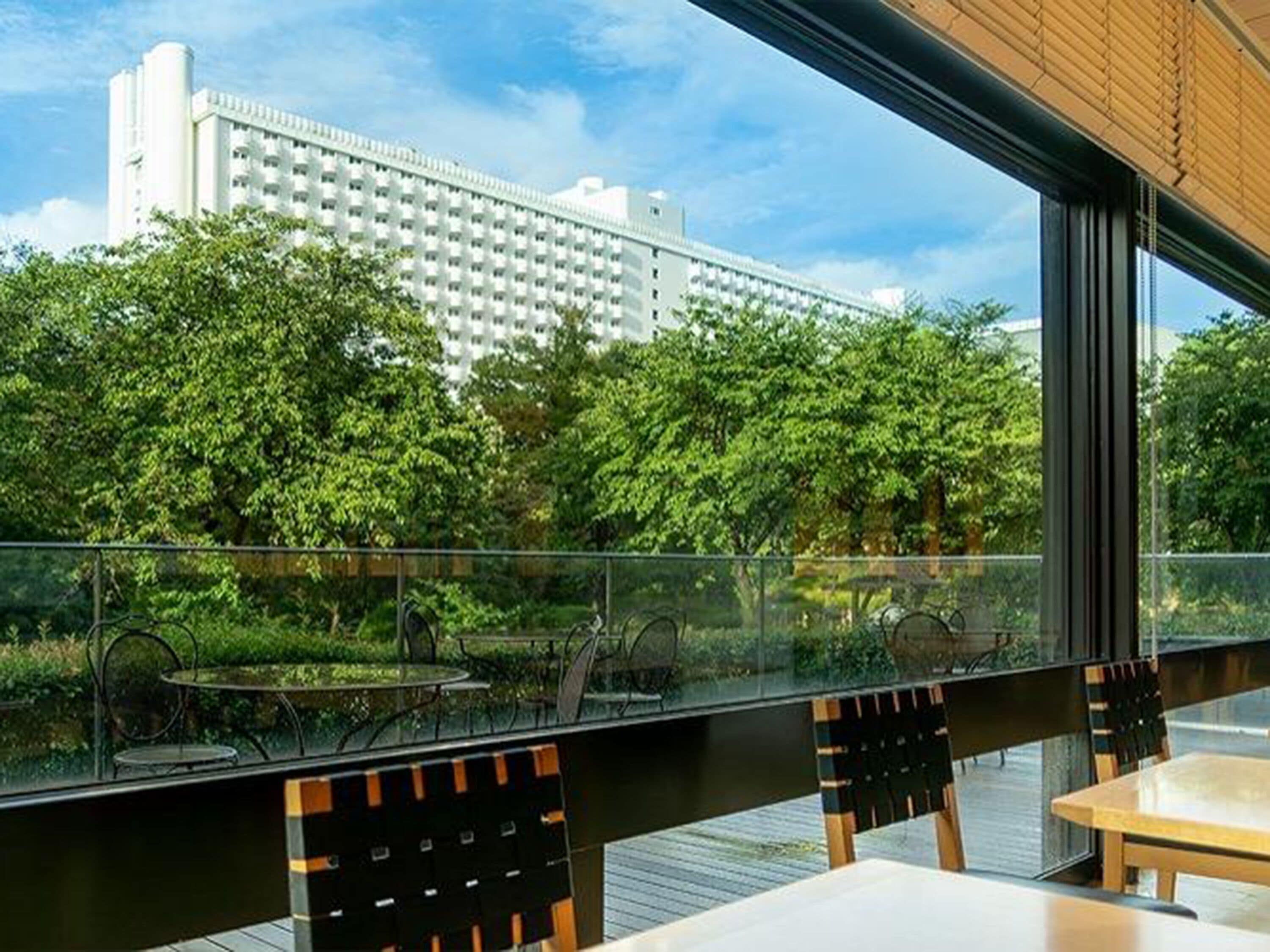 An outdoor seating area with tables and chairs, overlooking a lush green landscape and a large building in the background.