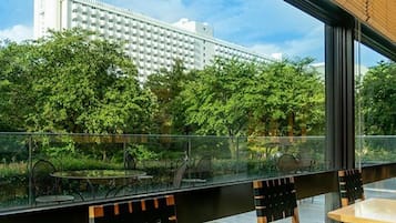An outdoor seating area with tables and chairs, overlooking a lush green landscape and a large building in the background.