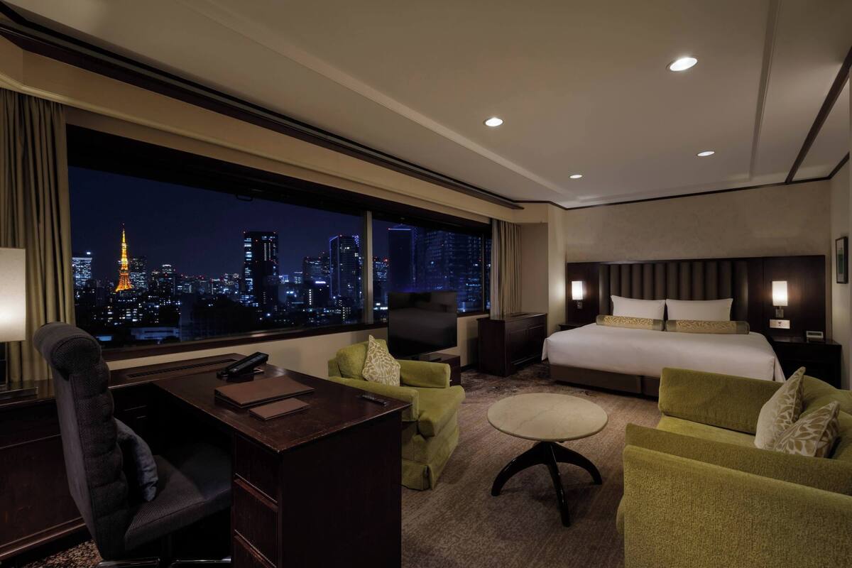 A hotel room with a large window, a bed, a desk, a chair, and a television.