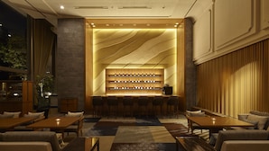 A modern bar area with a central shelf displaying bottles, surrounded by bar stools and seating.