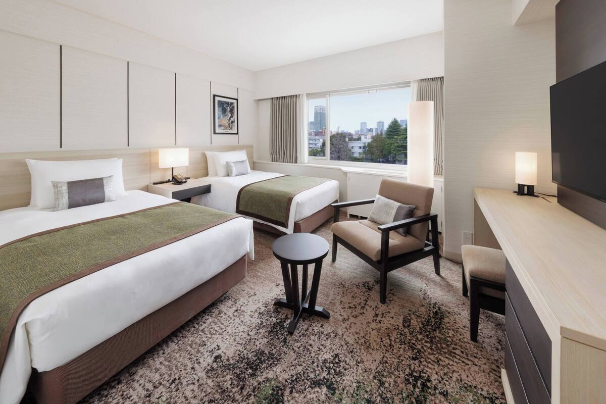 A hotel room with two beds, a desk, a chair, a small table, and a TV.