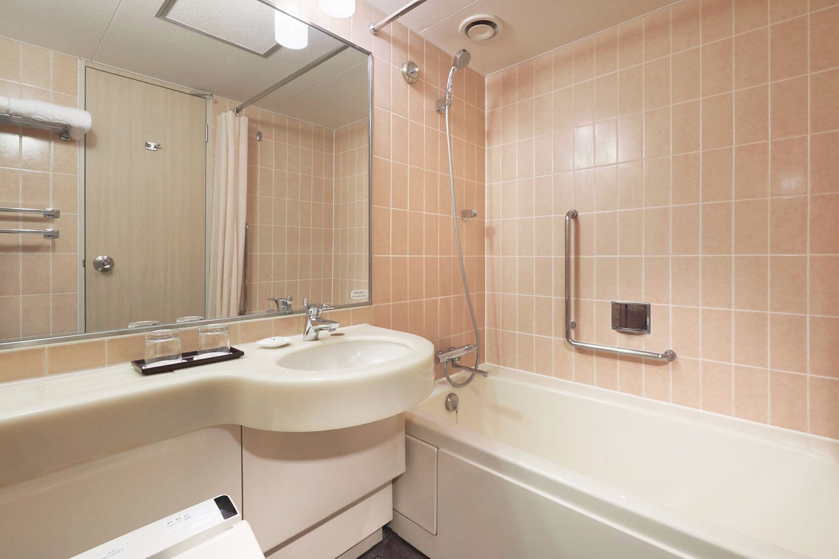 A bathroom with a sink, mirror, shower, and grab bars.