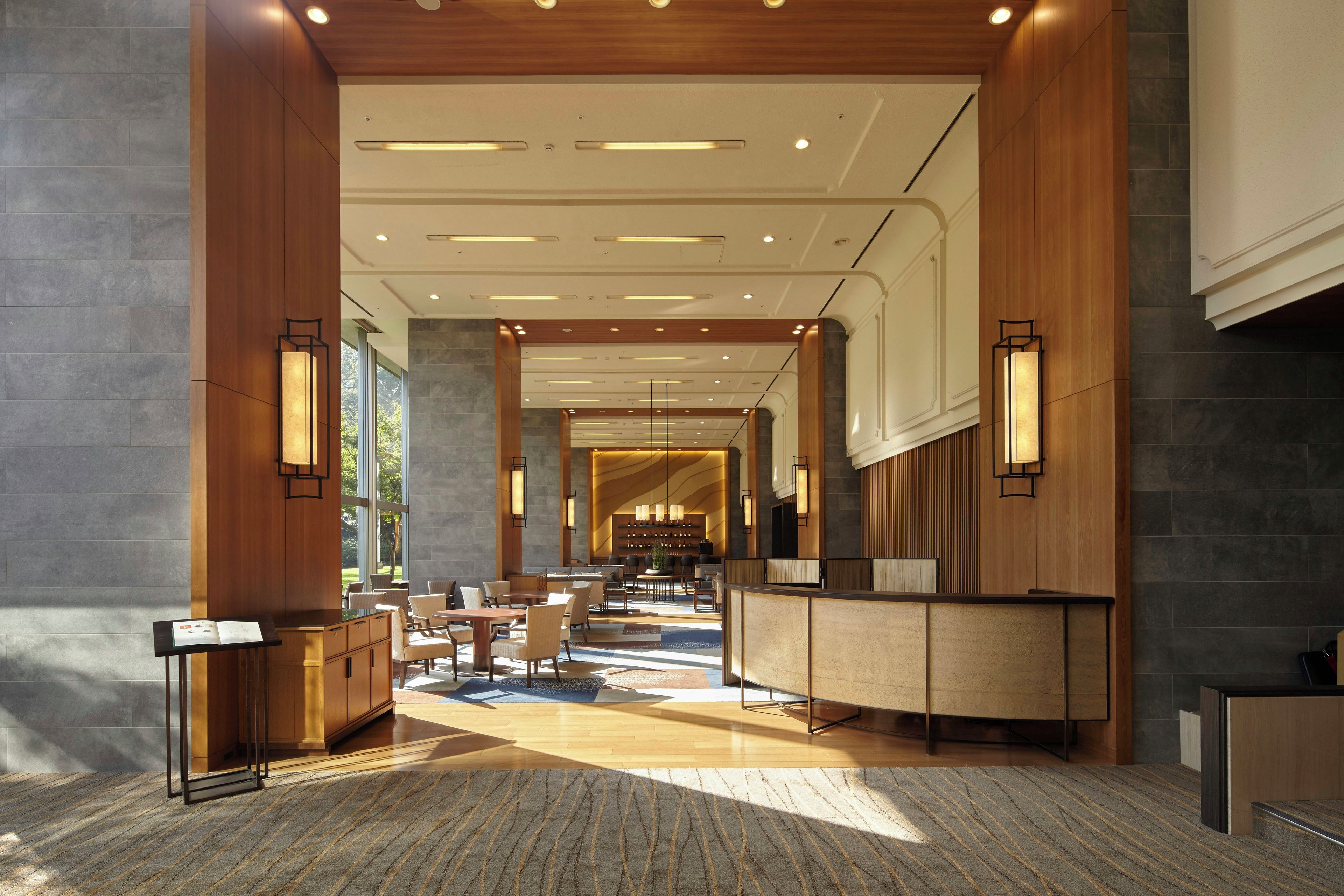 A spacious lobby with a reception desk, seating area, and a view of the outdoor garden.