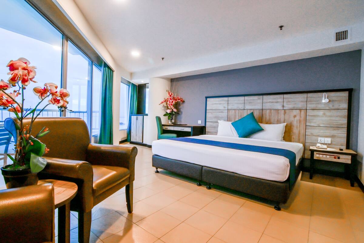 A hotel room with a large bed, a desk, a chair, and a potted plant.
