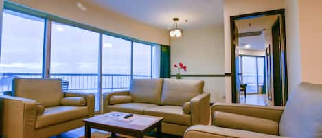 A spacious living room with a large window, a sofa set, a coffee table, and a small table with a vase of flowers.