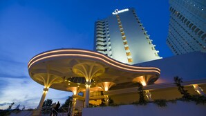 A modern hotel with a distinctive curved roof structure and a tall building in the background. - Flamingo By The Beach Penang (George Town)