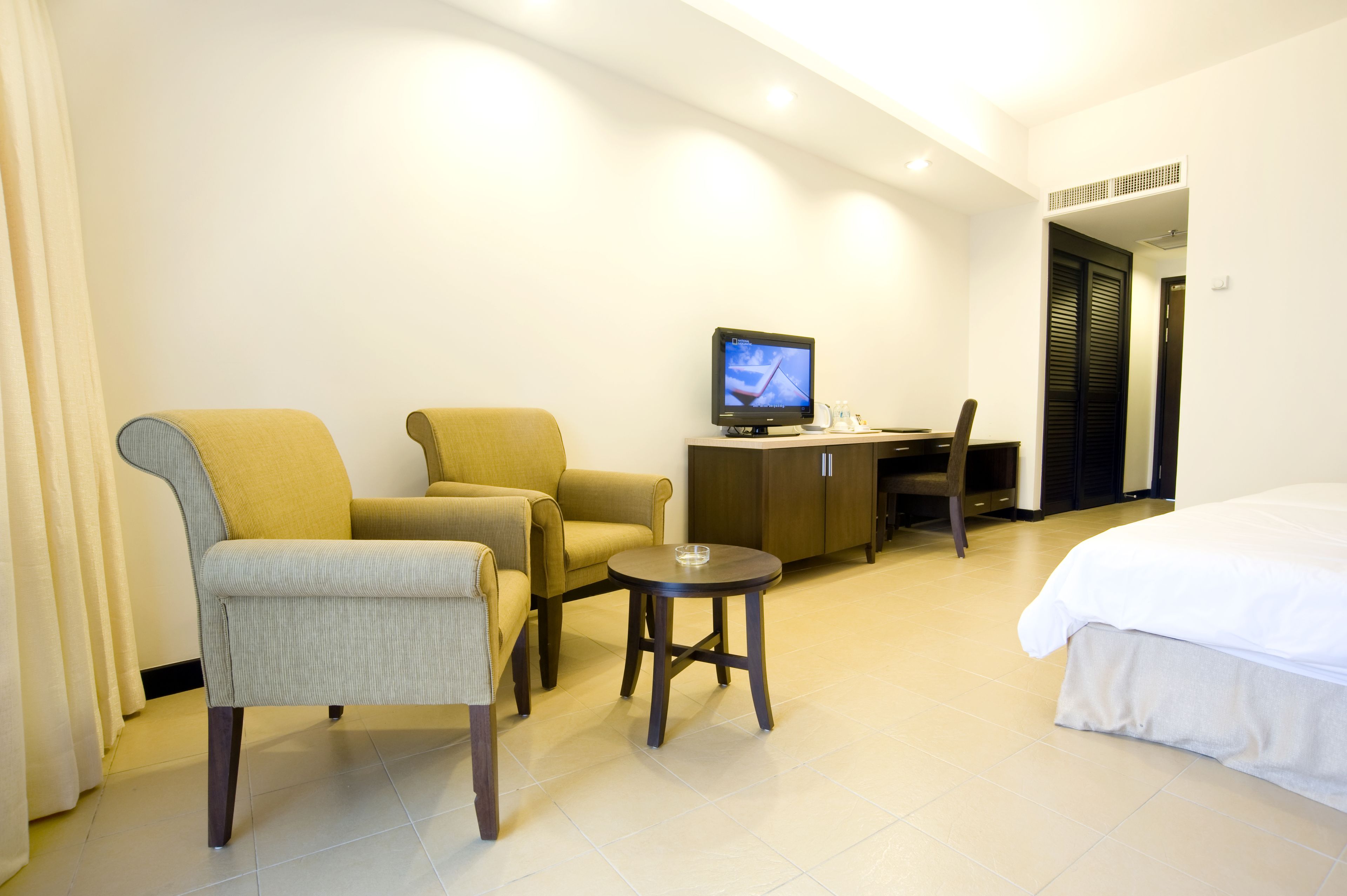 A hotel room with a bed, two armchairs, a small table, a television, and a desk.