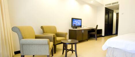 A hotel room with a bed, two armchairs, a small table, a television, and a desk.