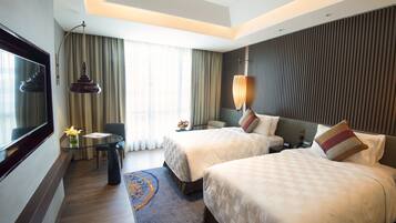 A hotel room with two beds, a TV, a desk with a lamp, and a view of the outdoors.
