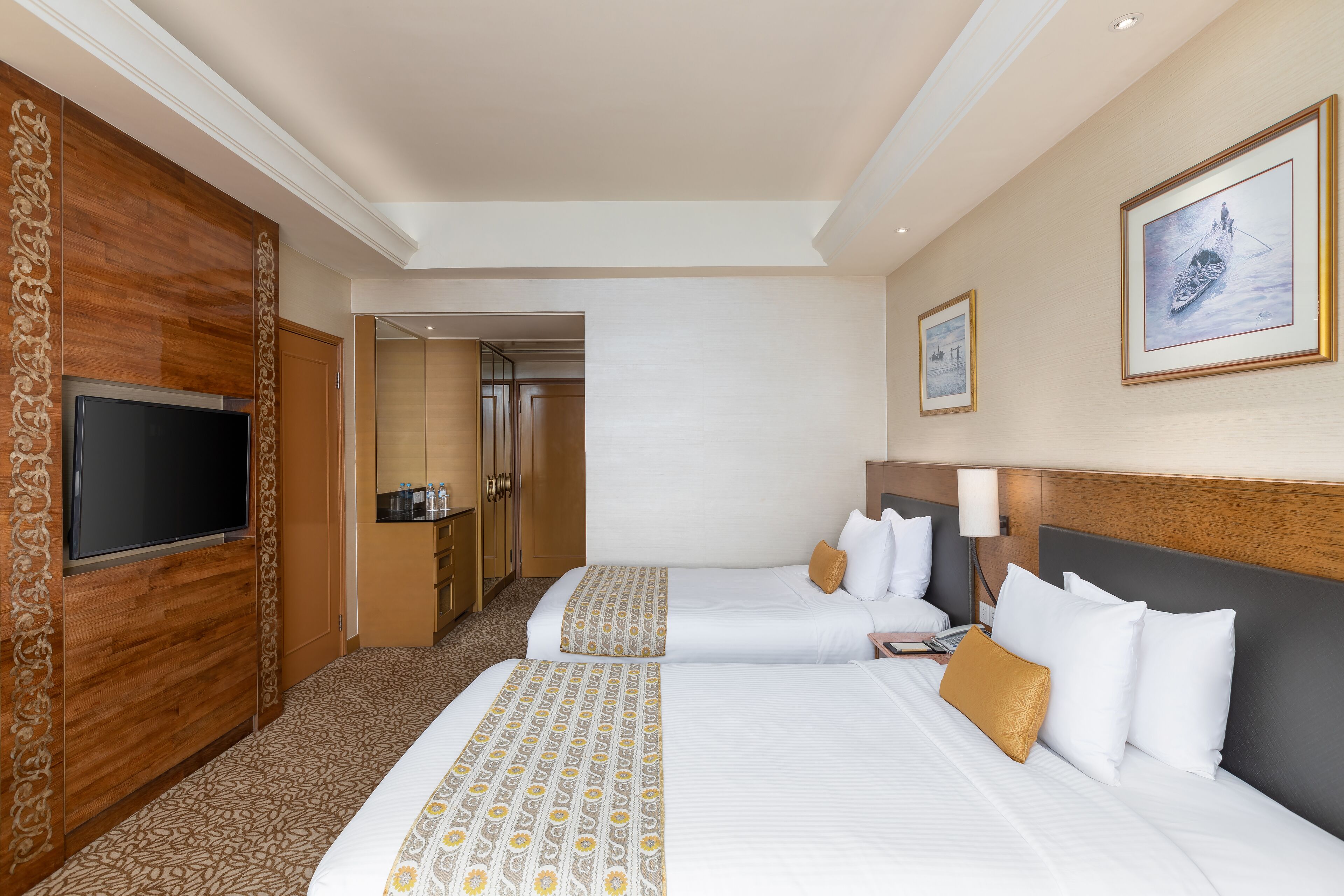 Habitación de hotel con dos camas, televisor, un panel decorativo de madera y cuadros en la pared.