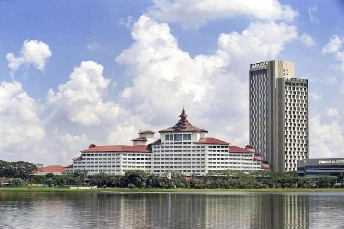 A large hotel with a central building and a tall adjacent tower, surrounded by water and greenery.
