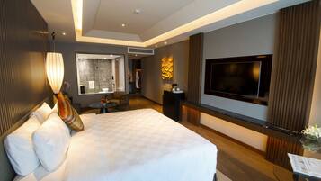 A modern hotel room with a large bed, a flat-screen TV, a seating area, and a bathroom visible through an open door.