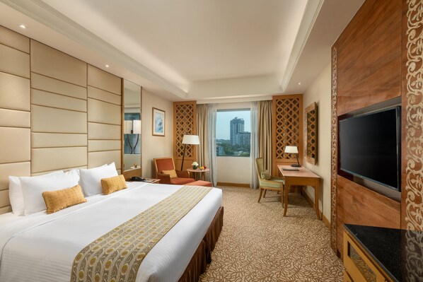 A hotel room with a large bed, a desk, a TV, and a view of the city.