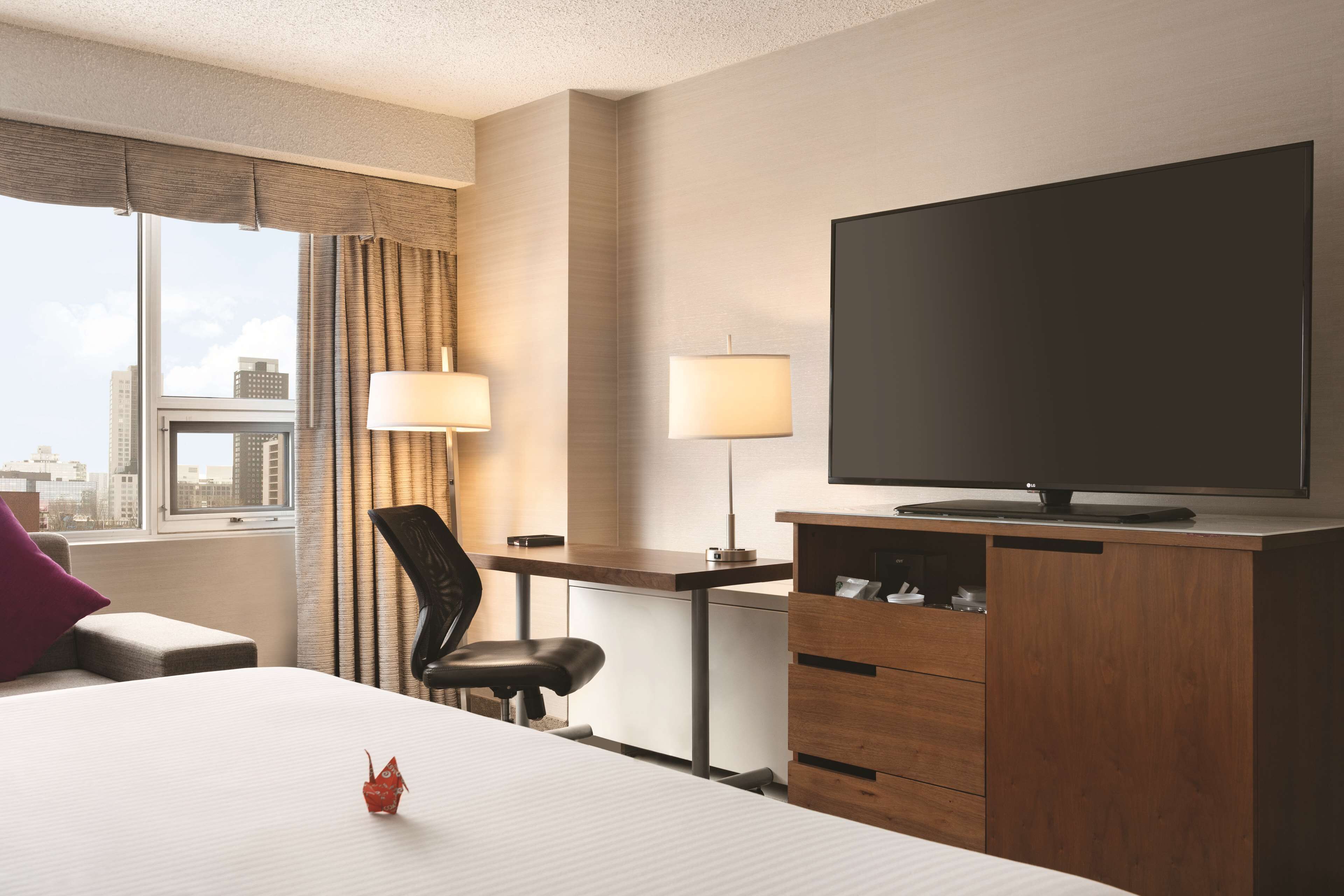 A hotel room with a bed, a desk, a chair, a television, and a window with curtains.