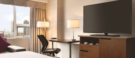 A hotel room with a bed, a desk, a chair, a television, and a window with curtains.