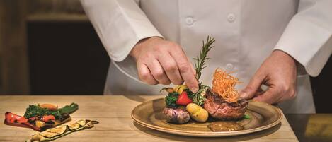 Un chef adornando un plato de comida con verduras y un bistec.