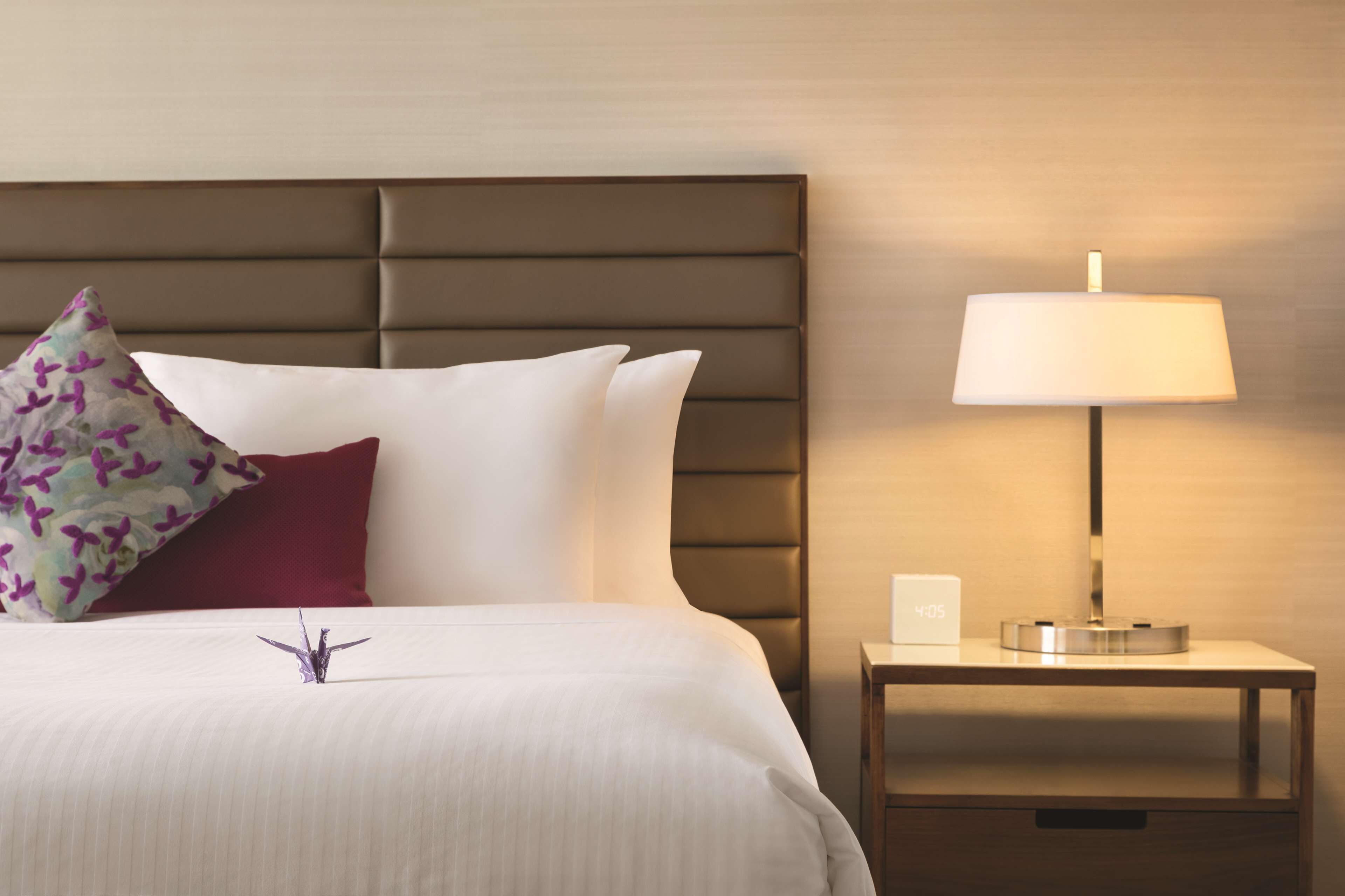 A neatly made bed with white linens, a decorative pillow, and a bedside table with a lamp.