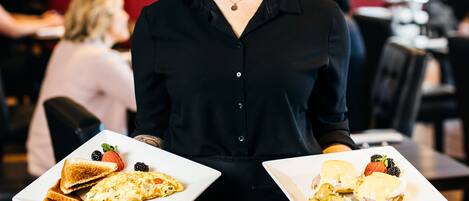 A person holding two plates of food in a restaurant setting.
