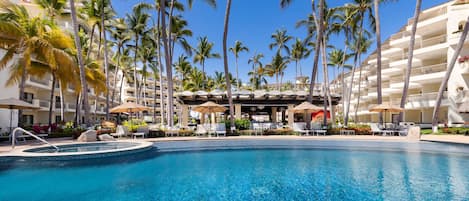 A hotel pool with clear blue water, surrounded by palm trees and lounge chairs.