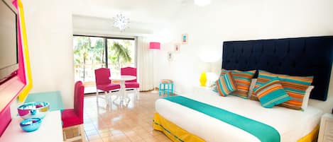 Une chambre d’hôtel lumineuse, dotée d’un grand lit, d’un ventilateur de plafond, d’un balcon avec une chaise rouge et d’un coin repas avec une chaise rose.