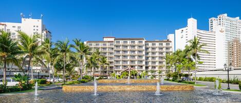 A hotel with a central courtyard featuring a fountain, surrounded by palm trees and a pool.