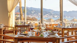 Una mesa de comedor dispuesta con platos, vasos y cubiertos, con vistas a un paisaje montañoso.