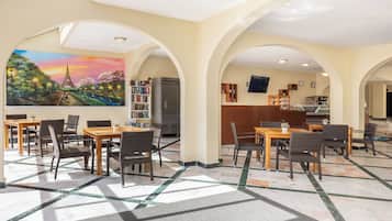 Een hotel lobby met een muurschildering van de Eiffeltoren, meerdere eettafels met stoelen, een koelkast en een keukenhoek.