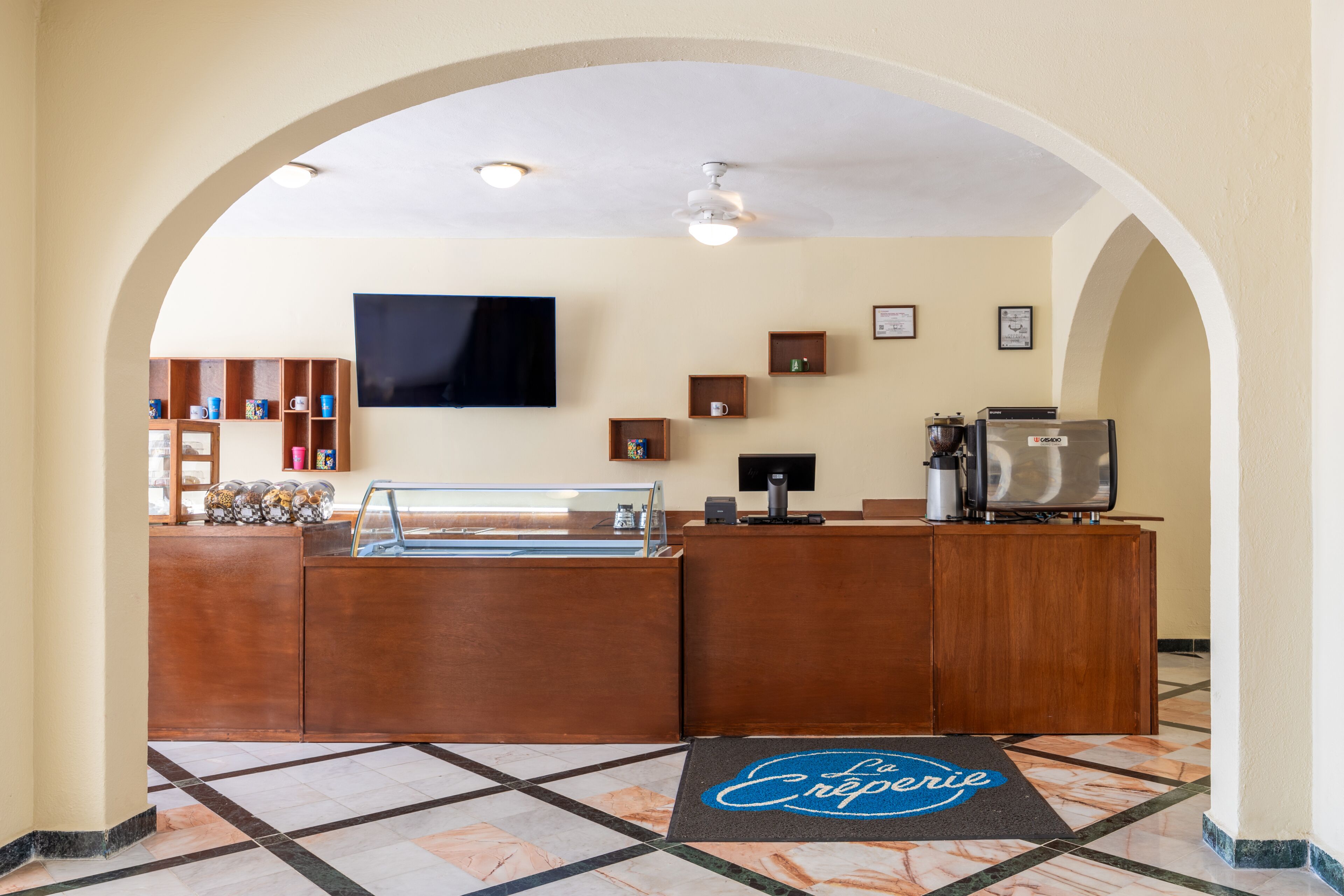 A reception area with a marble floor, wooden reception desk, a coffee machine, and a television mounted on the wall.