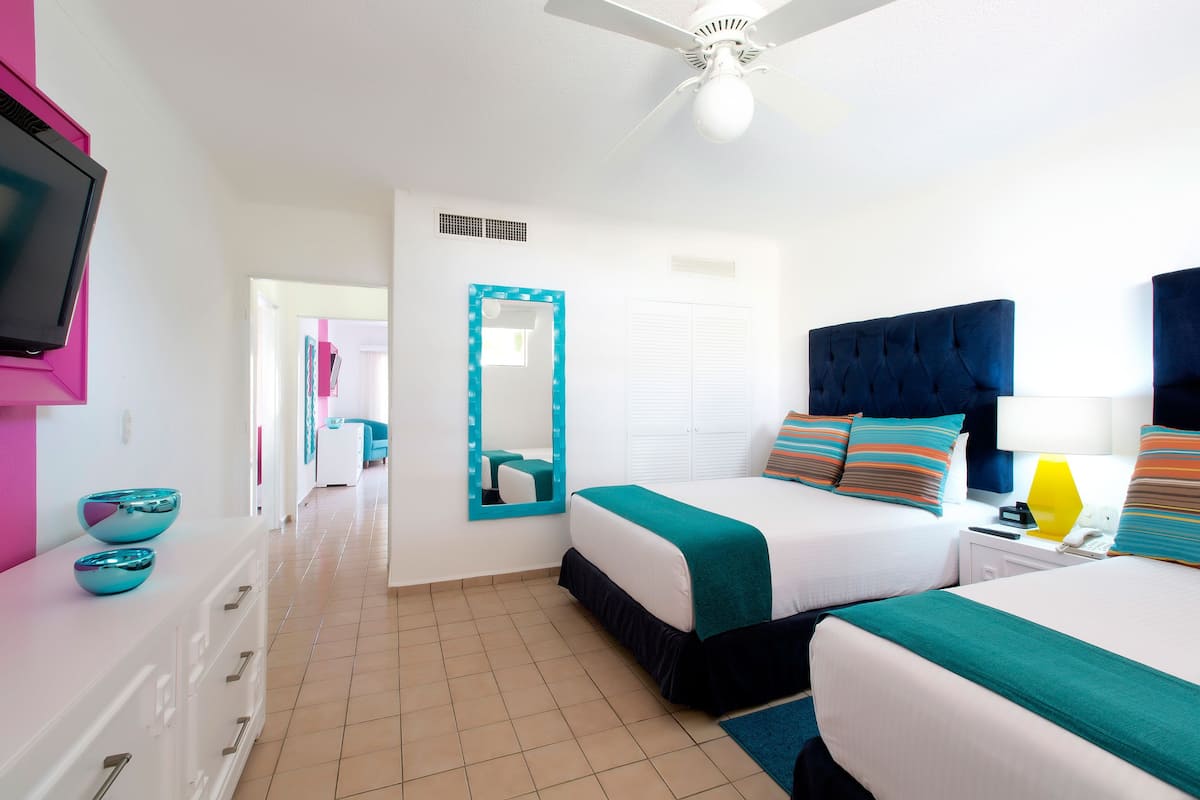 A hotel room with two beds, a television, a mirror, and a ceiling fan.