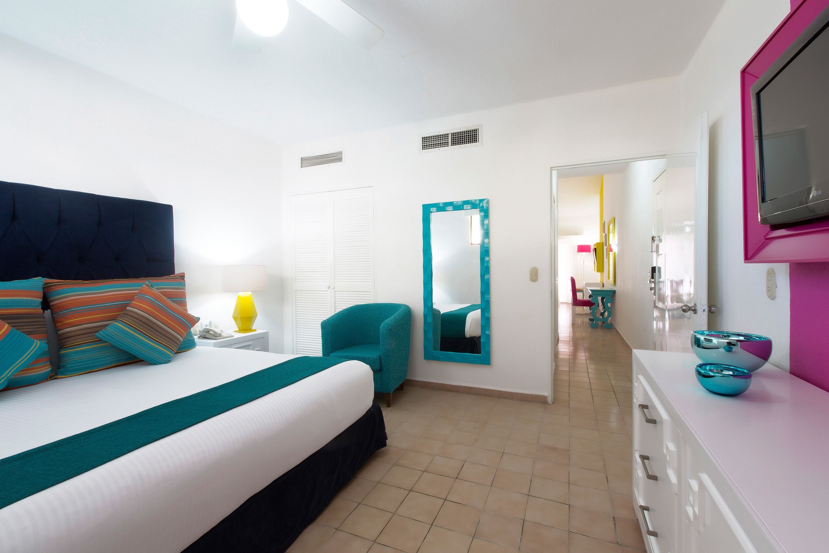 A hotel room with a bed, a chair, a mirror, a TV, and a dresser.