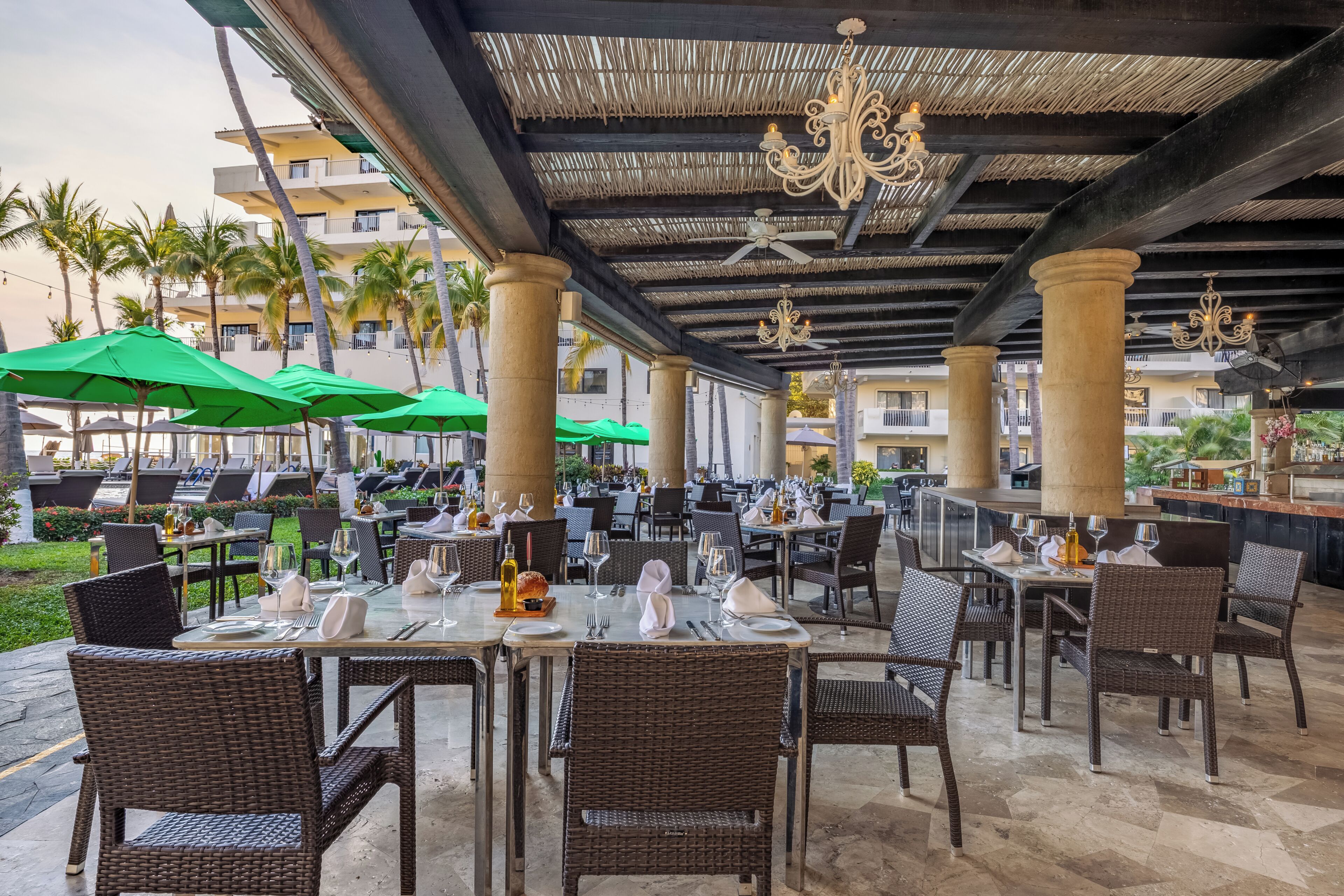 Un espace de restauration en plein air, avec des tables et des chaises, des parasols et une partie abritée dotée de colonnes et de lustres.