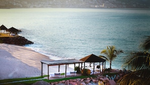 Un resort frente a la playa con un mirador, sillas de descanso y vistas al océano y colinas al fondo.