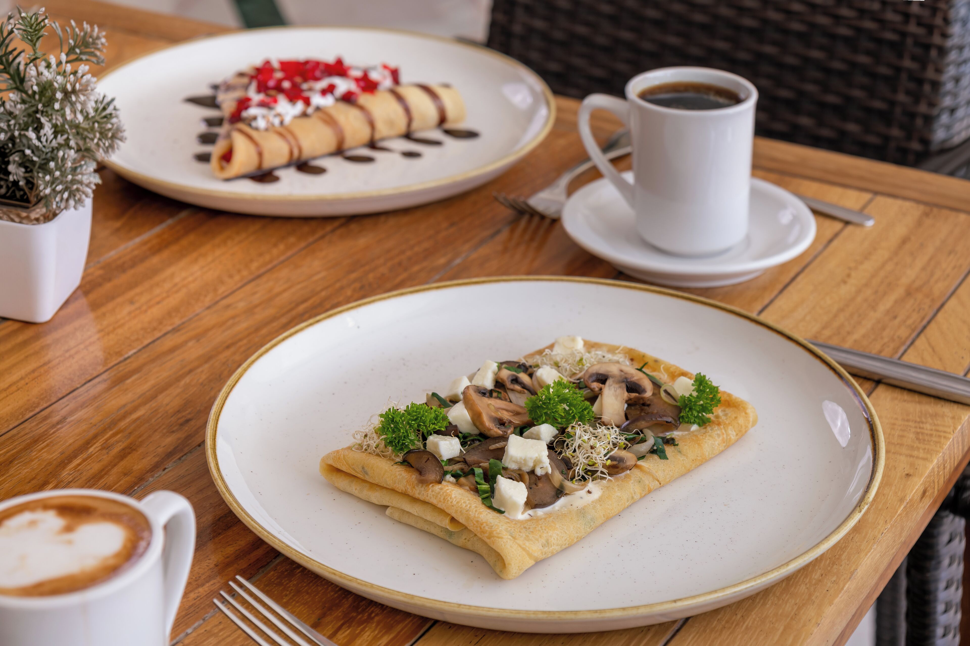 Um cenário de café da manhã com uma crepe, café e uma pequena planta sobre uma mesa de madeira.