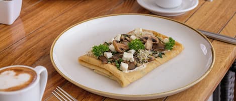 A breakfast setting with a crepe, coffee, and a small plant on a wooden table.