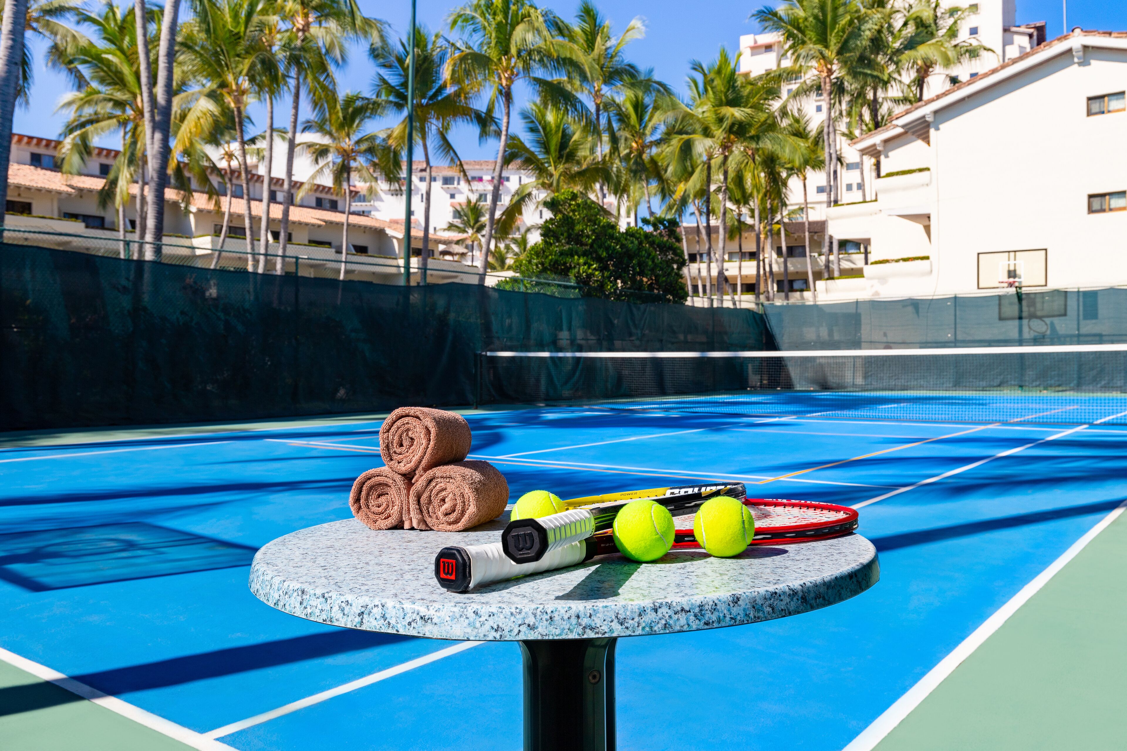 A tennis court with a table holding tennis balls, rackets, and towels.